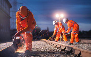 Railway maintenance workers using a grinder on a track at night